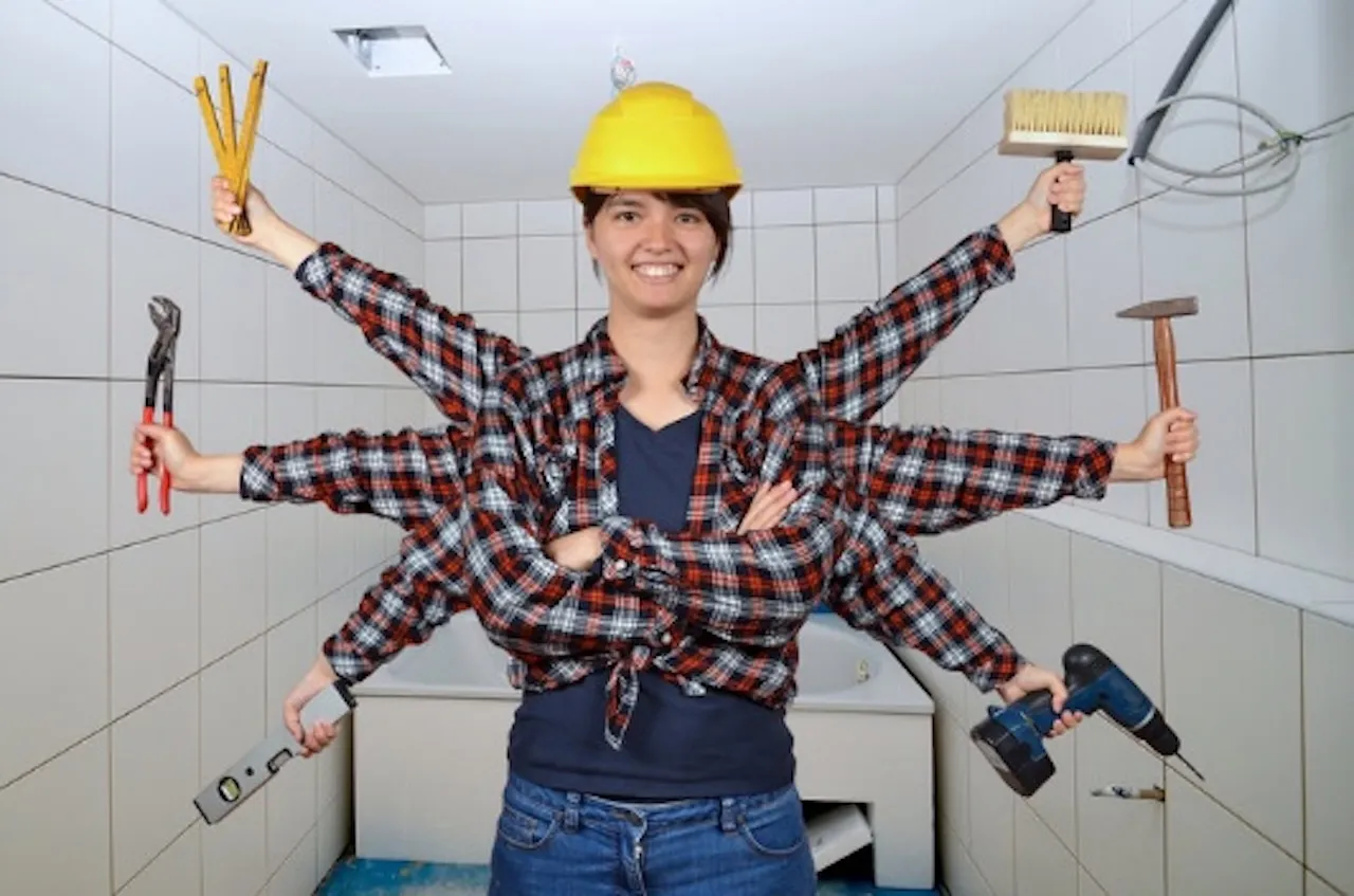 Sascha Stivic - eine Frau steht im Badezimmer mit Bohrmaschine, Hammer usw. in den Händen